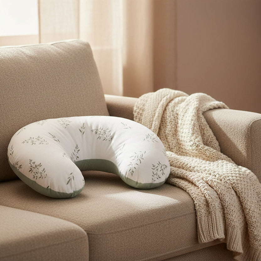 U-shaped pillow on a beige couch with a blanket and a glass of water in the background.